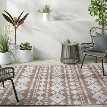Coastal patio scene with Metta Rust Area Rug, woven chairs, side table, and potted plants. Roomscene-Rectangle