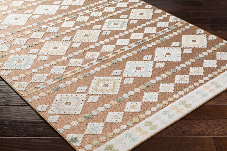 Close-up of the Metta Rust Area Rug showing diamond pattern in rust, cream, slate, green, and blue on dark wood floor. Corner