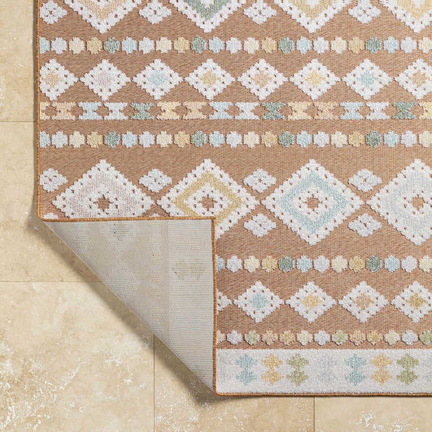 Close-up of the Metta Rust Area Rug showing rust, cream, blue, and green geometric pattern and woven texture. Fold