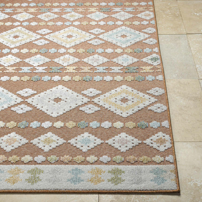 Close-up of Metta Rust Area Rug showing geometric diamond pattern in rust, cream, blue, and green on tile floor. Front