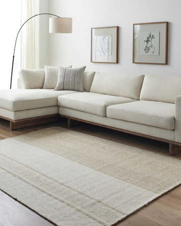 Living room scene with a neutral sectional sofa and the striped Myrna Area Rug in ash, off white, and tan. Roomscene-Rectangle