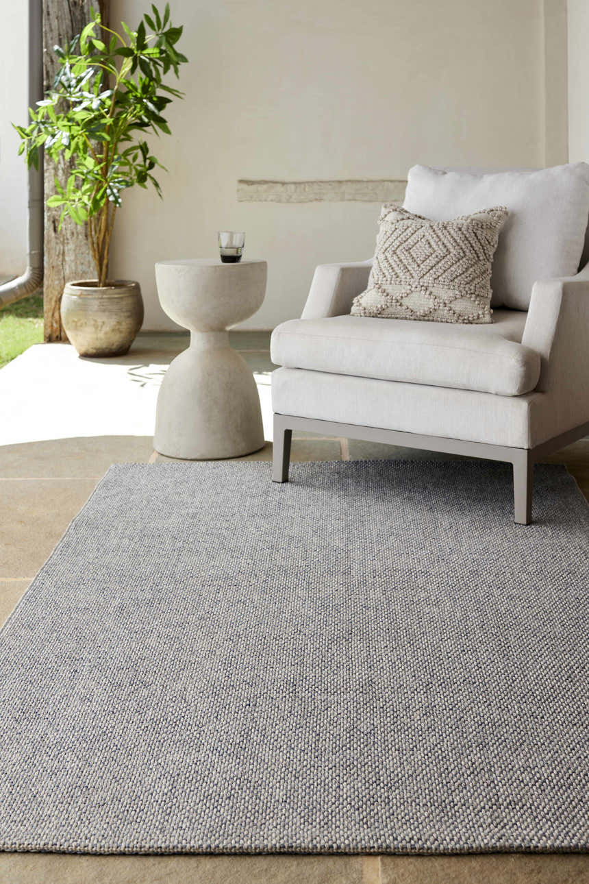 Neutral patio scene with a gray Mirit Area Rug, white chair, and stone side table. Roomscene-Rectangle