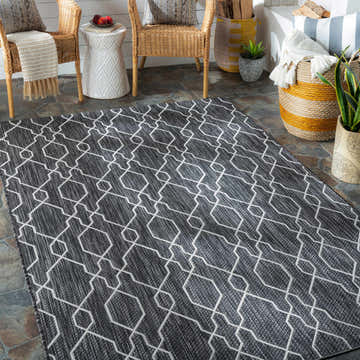Patio scene with a charcoal and cream geometric Naco Area Rug, wicker chairs, and natural textures. Roomscene-Rectangle
