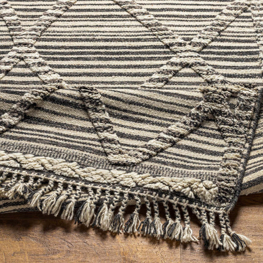 Close-up of the Nairobi Area Rug, a hand-knotted wool rug with black, gray, and ivory stripes and fringe. Fold