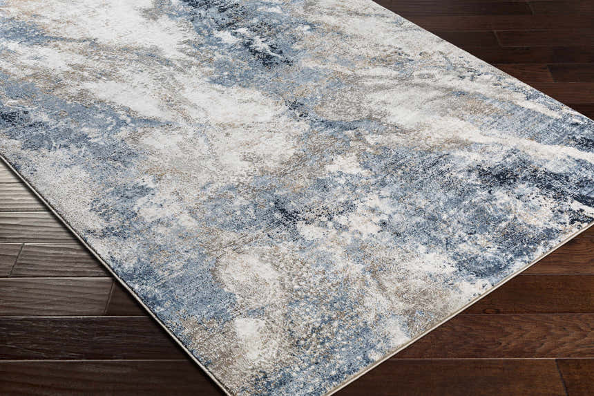 Close-up of the Napierville Blue Marble Rug showing its charcoal, blue, ivory, and tan abstract design on dark wood floors. Corner