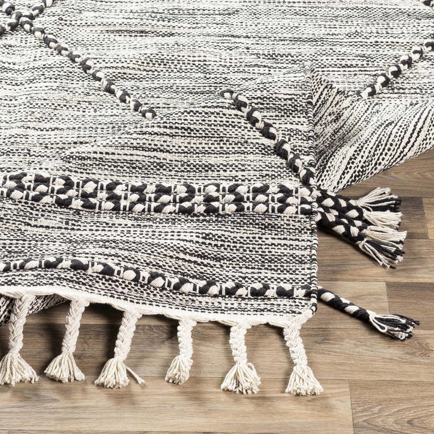 Close-up of the Neal Black/Cream Trellis Cotton Rug, showing the hand-woven texture and tassel details. Fold