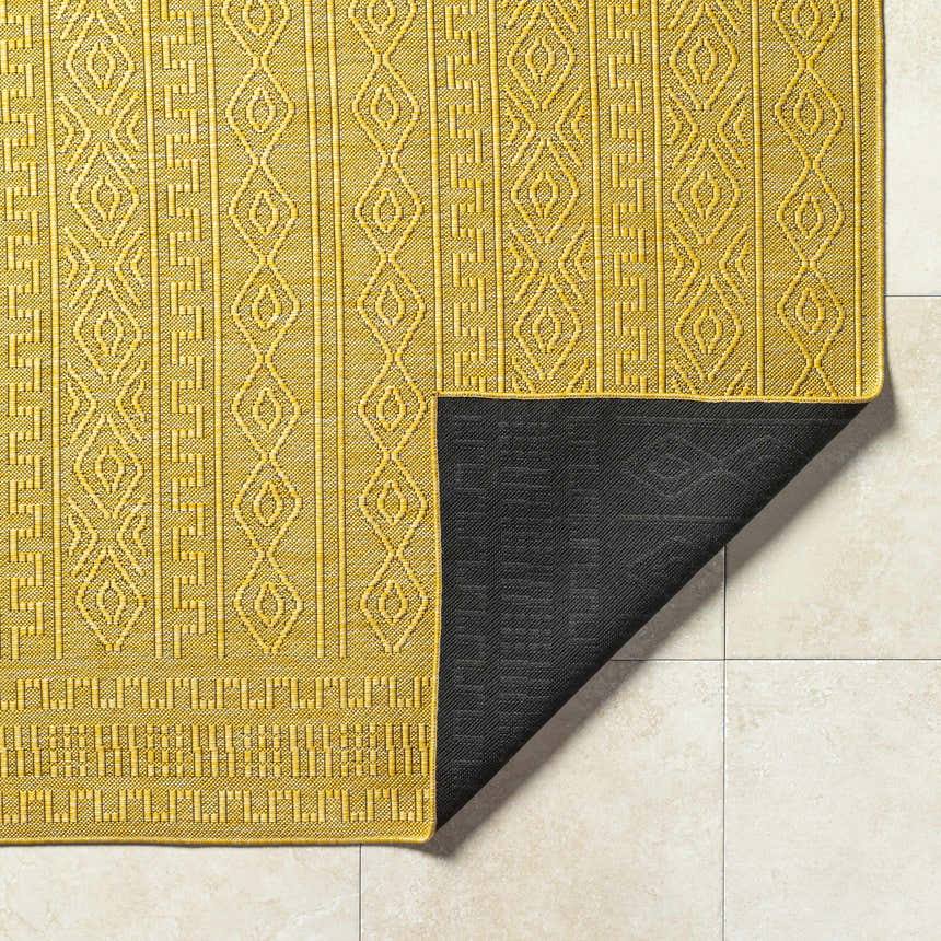 Close-up of the Nuela Mustard Area Rug showing the geometric pattern and black backing. Fold