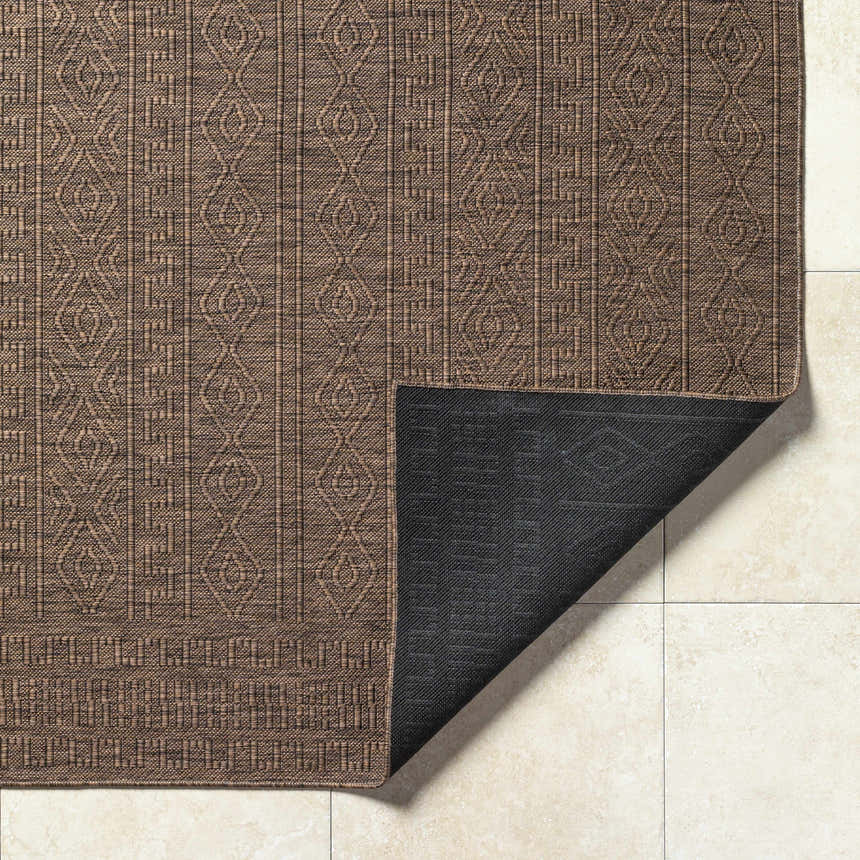 Close-up of the Nuela Dark Brown Area Rug showing its geometric pattern and dark brown color on a cream tile floor. Fold