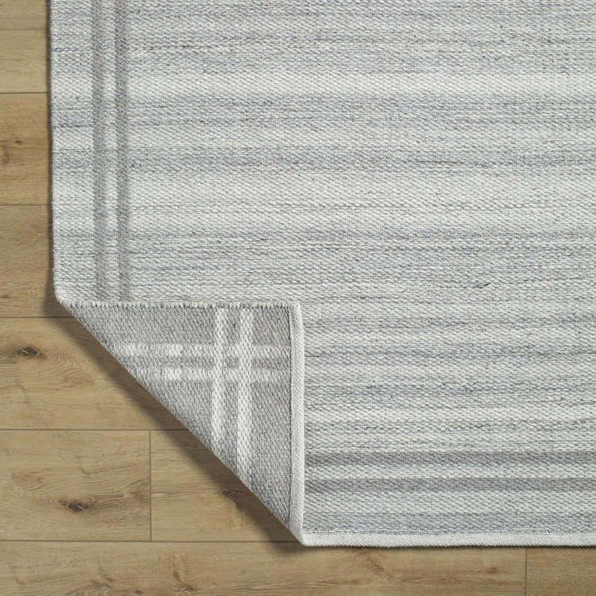 Close-up of the hand woven Nimue Gray Area Rug showing its wool texture and gray and ivory stripes on wood floors. Fold