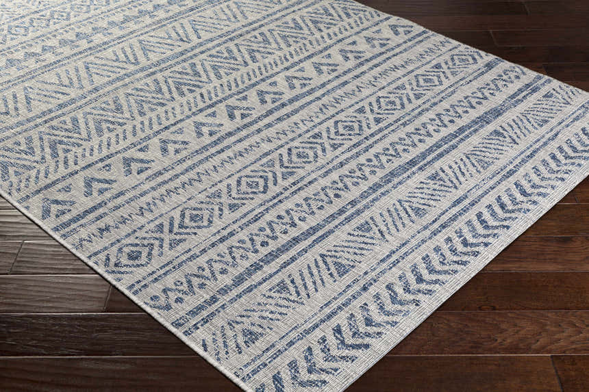 Close-up of the Novato All Over Pattern Performance Rug. Blue geometric design on a light background. Machine woven texture. Corner