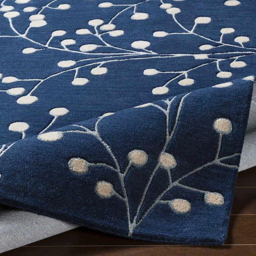 Close-up of the Blue Elsu Area Rug showing its ink blue wool texture and floral design in tan and cream. Fold