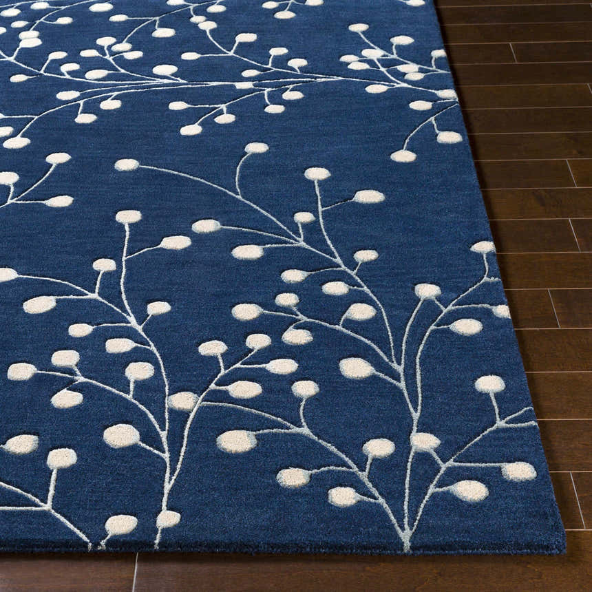 Close-up of the Blue Elsu Area Rug, a hand-tufted wool rug with a floral pattern in ink blue and tan on dark wood floors. Front