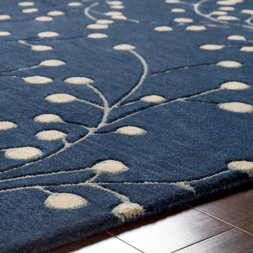 Close-up of the Blue Elsu Area Rug showing its ink blue wool texture and tan floral design on a hardwood floor. Texture