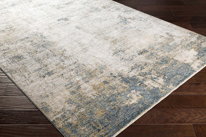 Close-up of the Odell Abstract Luxe Fringe Rug in dark blue, light blue, gray, and mustard on a dark wood floor. Corner