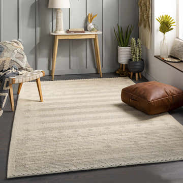 Neutral living room with a light beige Odem Area Rug, wood accents, leather pouf, and potted plants. Roomscene-Rectangle