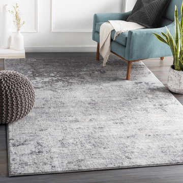 Living room scene with a gray Ortonville Abstract rug, teal chair, and knit pouf. Roomscene-Rectangle