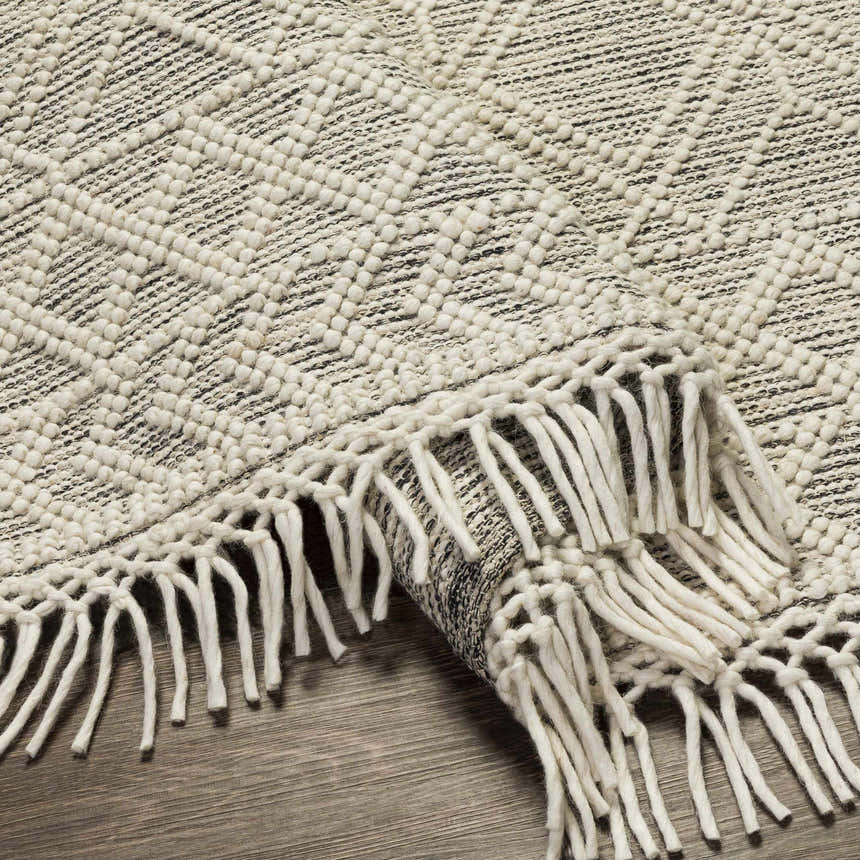 Close-up of the Ossun Wool Rug with Tassels. Cream geometric pattern on black woven rug. Farmhouse style with fringe. Fold