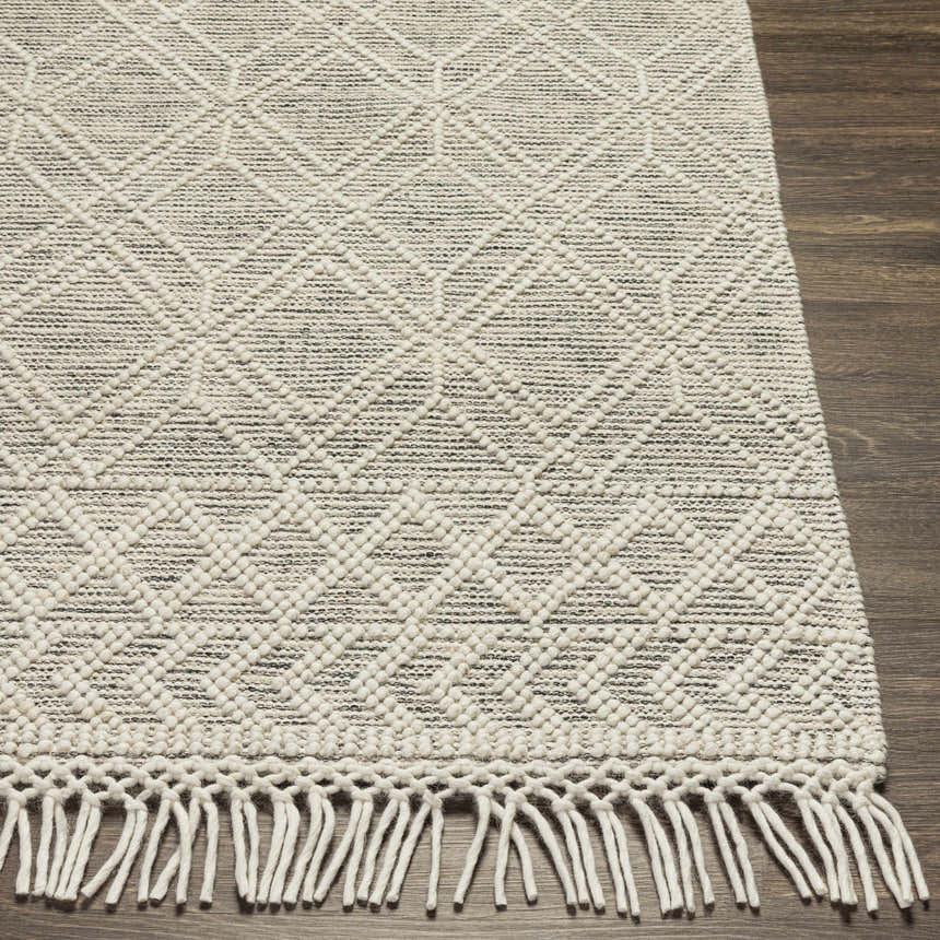Close-up of the hand woven Ossun Wool Rug with Tassels, showing cream geometric pattern and black accents on a wooden floor. Front