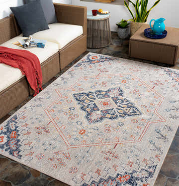 Outdoor patio scene with a Papineauville area rug in aqua, cream, and blue, styled with wicker furniture and slate tile flooring. Roomscene-Rectangle