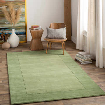 Living room scene with a Bordered Solid Green Wool Rug, wood chair, and decorative vases. Roomscene-Rectangle