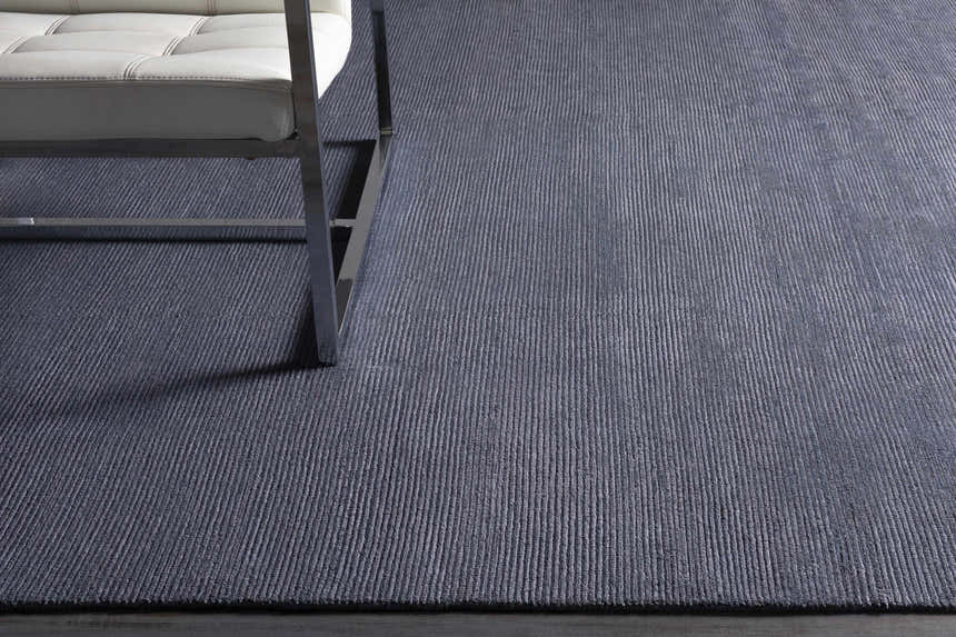 Close-up of Philipsburg Carpet in dark blue with a subtle striped texture and a modern white chair. Styleshot
