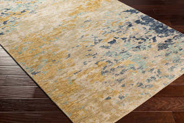 Close-up of the Pias Area Rug showing its beige, gray, and blue contemporary pattern and hand-knotted texture on dark wood floor. Corner