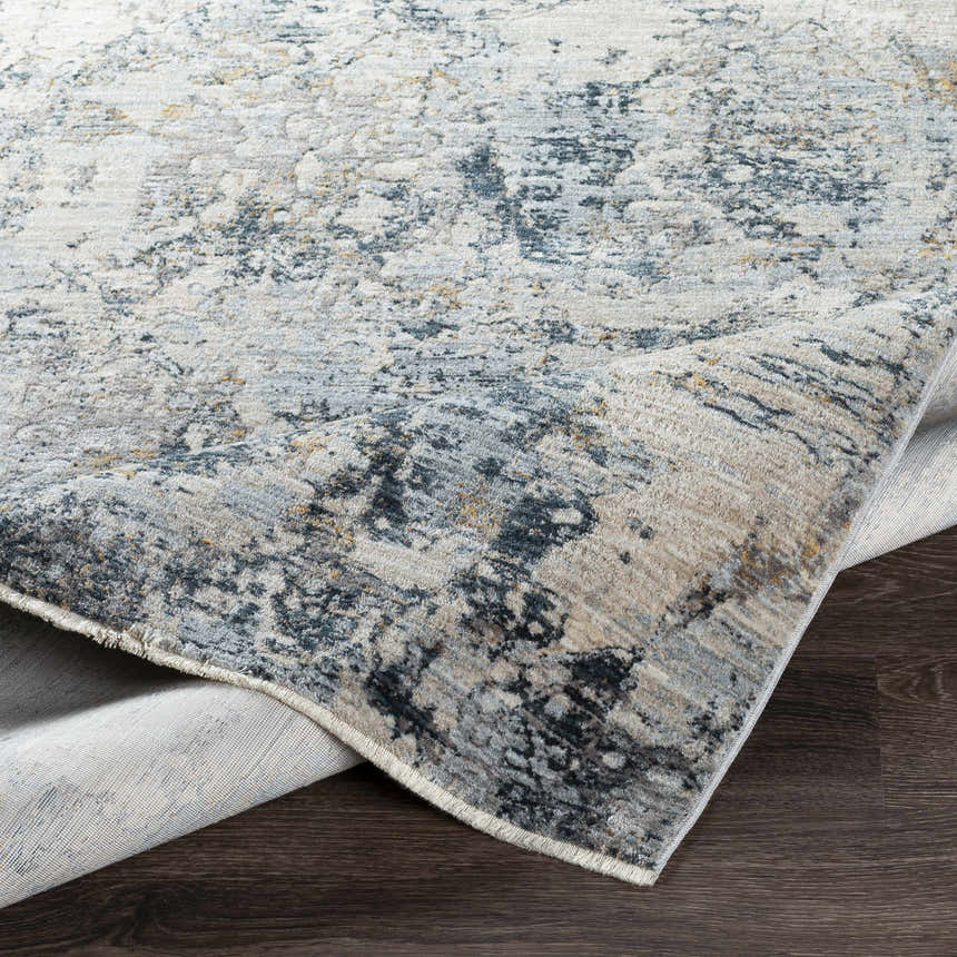 Close-up of the Pinjarra Luxe Rug. Abstract design in charcoal, cream, dark blue, gray, and tan on a polyester rug. Fold