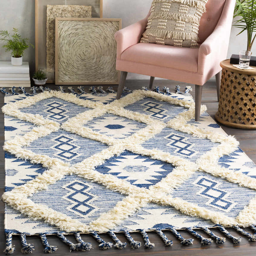 Living room scene with Painesdale Blue/White Wool Carpet, pink chair, and bohemian decor. Tasseled rug adds texture. Roomscene-Rectangle