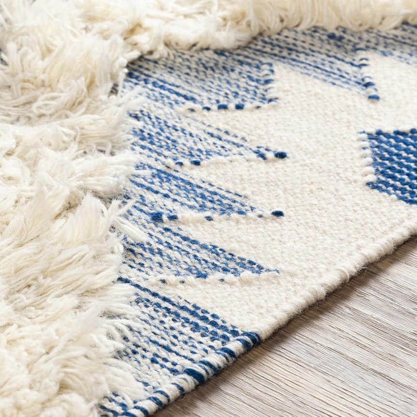 Close-up of Painesdale Blue/White Wool Carpet showing ivory fringe and woven dark blue geometric pattern. Texture