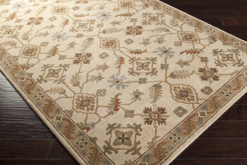 Close up of the Postelle Wool Rug. Beige rug with brown, sage, and blue floral and geometric pattern. Corner