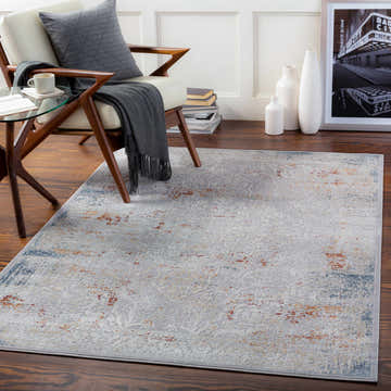 Living room scene with Petersburgh Textured Luxe Area Rug in gray, brick red, camel, and blue tones under a modern chair and glass table. Roomscene-Rectangle