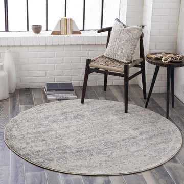 Living room scene with a round Rachel Area Rug in charcoal, gray, and beige tones on a gray wood floor. Roomscene-Round