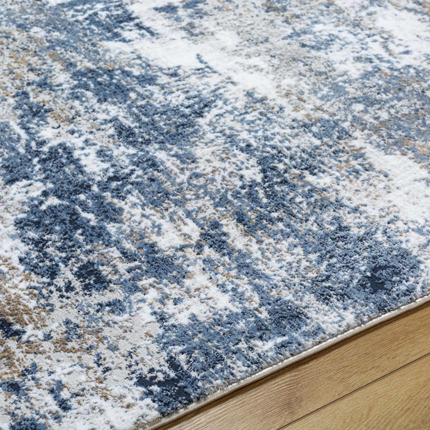 Close-up of the Ord Area Rug showing its abstract pattern in denim, ivory, and tan on a wood floor. Texture