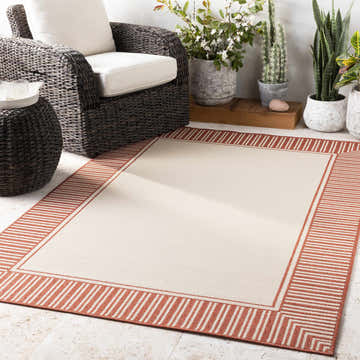 Patio scene with Redby Area Rug. Beige rug with brick red striped border, wicker furniture, and potted plants. Roomscene-Rectangle