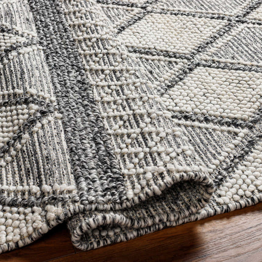 Close-up of the hand woven Rehn Area Rug showing its dark gray, light gray, and taupe geometric pattern and textured recycled PET yarn. Fold