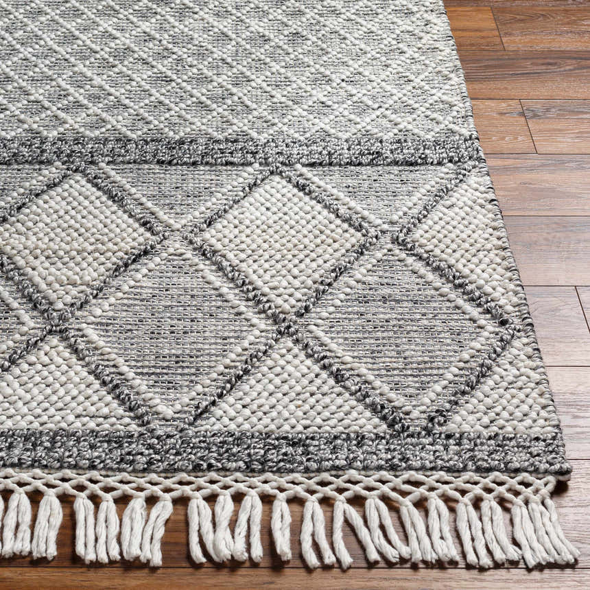 Close-up of the Rehn Area Rug. Dark gray and light gray diamond pattern with fringe on a wood floor. Hand woven texture. Front