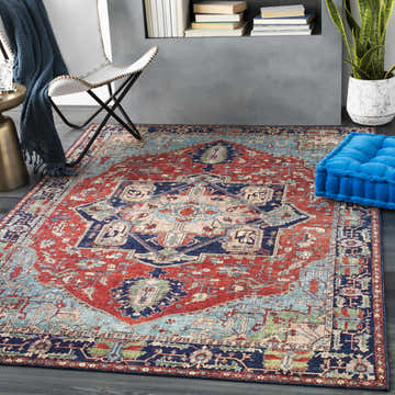 Living room scene with a Ripplemead Area Rug in red, blue, and green. Styled with a chair, blue throw, and floor cushion. Roomscene-Rectangle