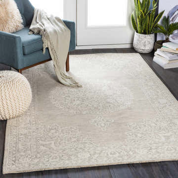 Living room scene with a Roessleville Cream Wool Area Rug, blue chair, knit pouf, plants, and dark wood floors. Calm and inviting. Roomscene-Rectangle