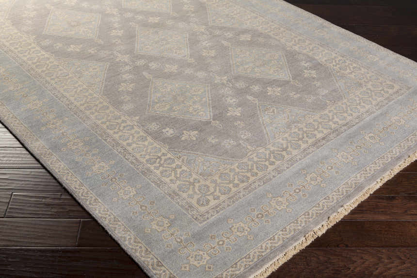 Close up of the hand-knotted Roma Area Rug. Medium gray and taupe wool rug with traditional floral and diamond pattern. Corner