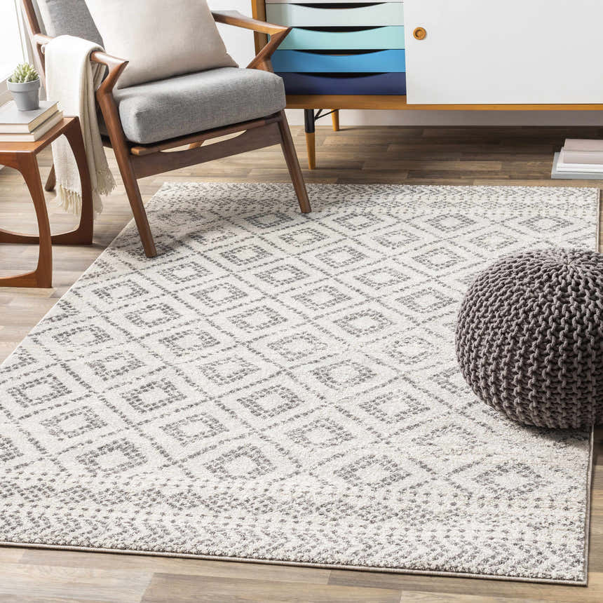 Living room scene with a gray chair, pouf, and the Romeoville Area Rug in charcoal, gray, and white. Roomscene-Rectangle