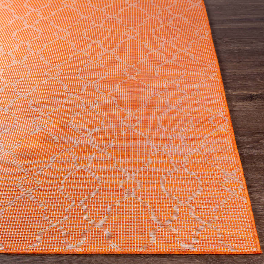 Close-up of the Rowde Flatweave Area Carpet in burnt orange with a geometric pattern on dark wood flooring. Front