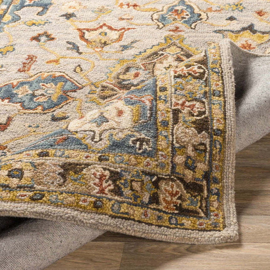 Close-up of the hand-tufted Rozel Area Rug. Features a traditional oriental pattern in brown, blue, and beige wool. Fold