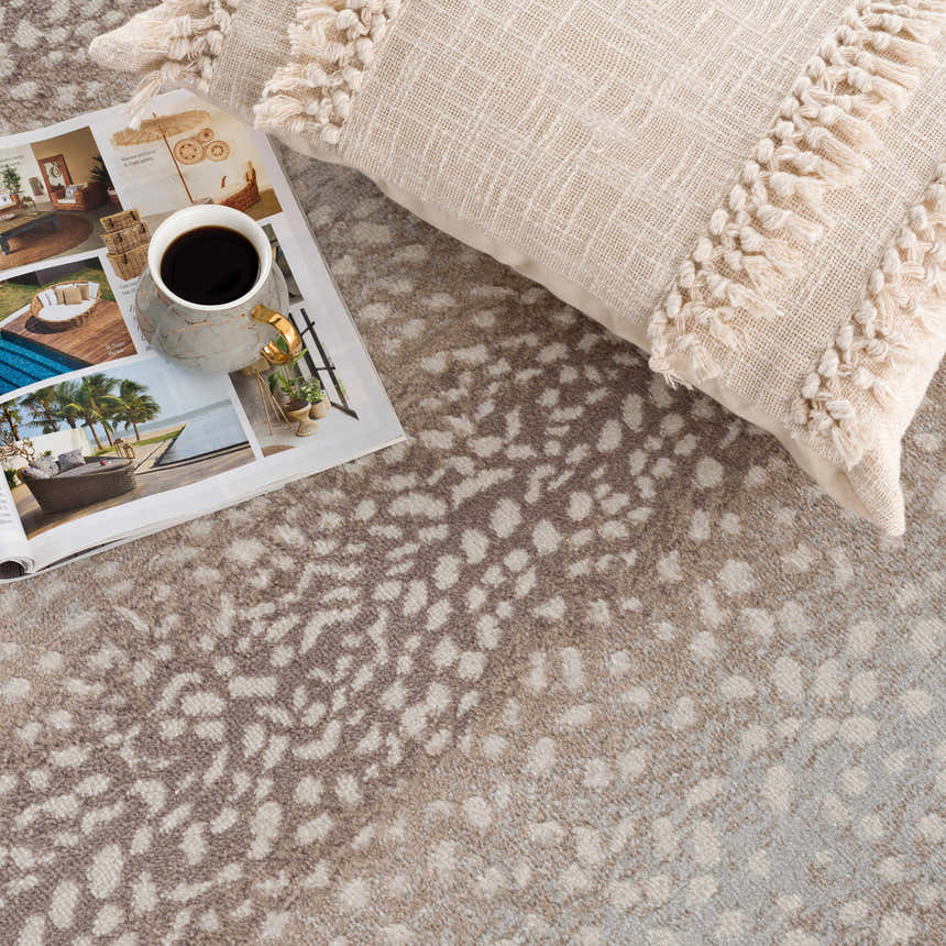 Close-up of Pointblank Tan Leopard Print Rug with ivory pillow and magazine, showcasing the rug's animal print design. Styleshot