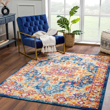 Living room scene with a blue velvet chair and the Istanbullu Orange Area Rug, a vintage style rug with gold and navy accents. Roomscene-Rectangle