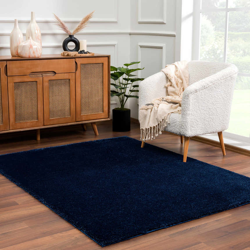 Living room scene with a Navero Dark Blue rug, wood cabinet, and white chair. Roomscene-Rectangle