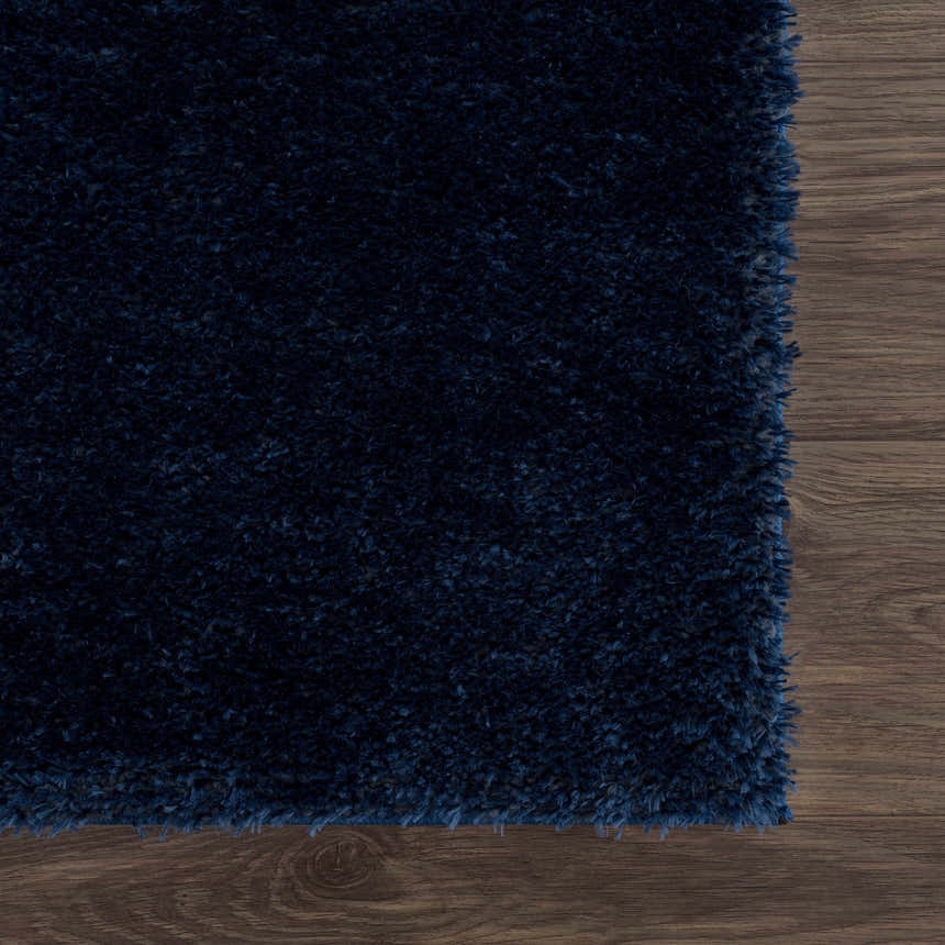 Close-up of the plush, dark blue Navero shag rug on a wood floor. Shows texture and color. Swatch
