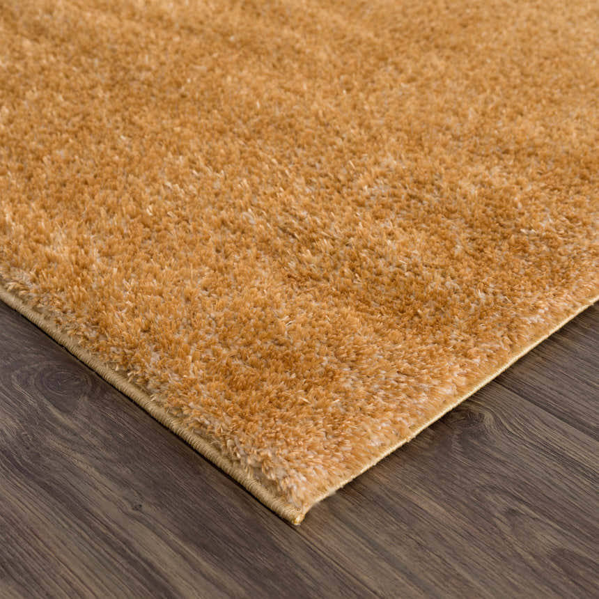 Close-up of a Heavenly Solid Mustard Plush Rug showing its soft texture and color on dark wood flooring. Corner