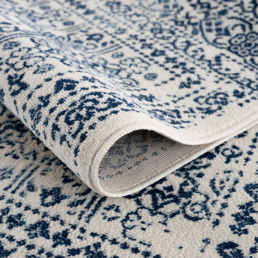 Close-up of the Michie Blue Area Rug showing its dark blue and white bohemian pattern and machine woven texture. Fold