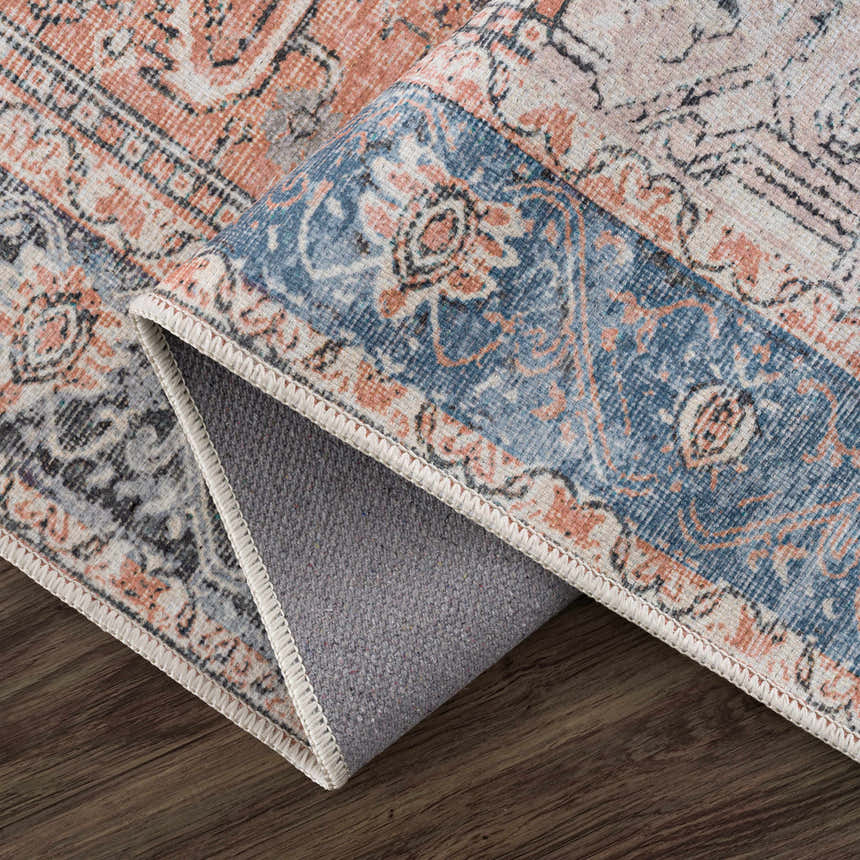 Close-up of the Rosman Distressed Washable Area Rug showing its beige, blue, and brick red oriental pattern and chenille texture. Fold