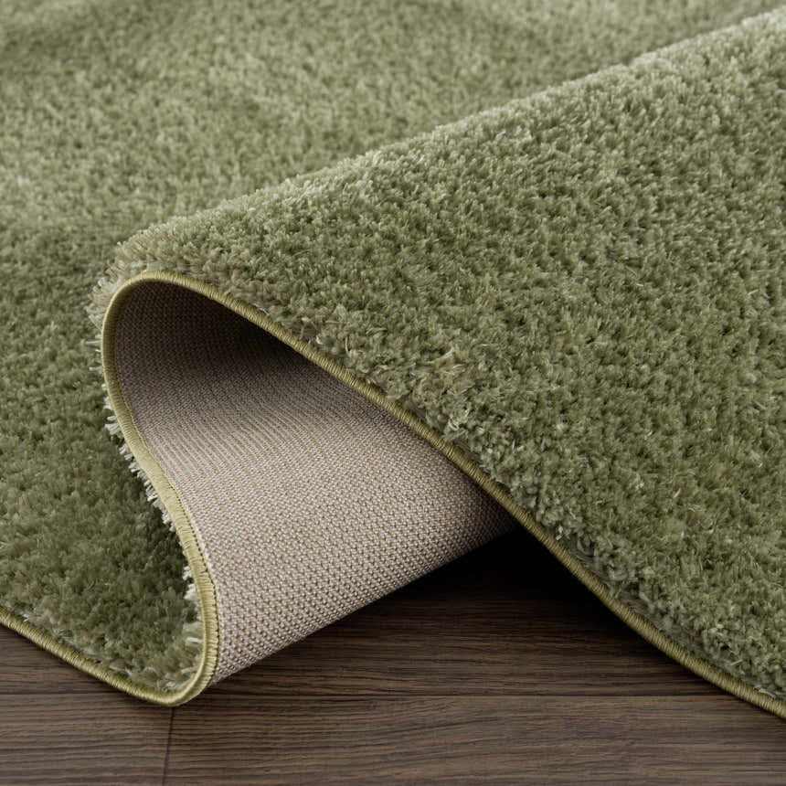 Close-up of the plush texture and backing of the Heavenly Solid Green Plush Rug on a dark wood floor. Fold